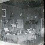 View of an interior with wooden tables, maps of the Congo on the wall as well as a small piano