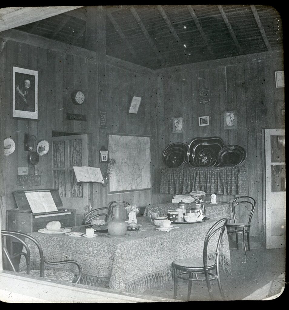 View of an interior with wooden tables, maps of the Congo on the wall as well as a small piano