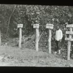 A village graveyard with simple graves marked with wooden posts and name plaques