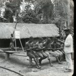 Locals assembled outside a village schoolhouse with a graph of English alphabetical characters in view