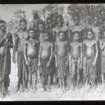 A group of assembled locals with simple loincloths and spears