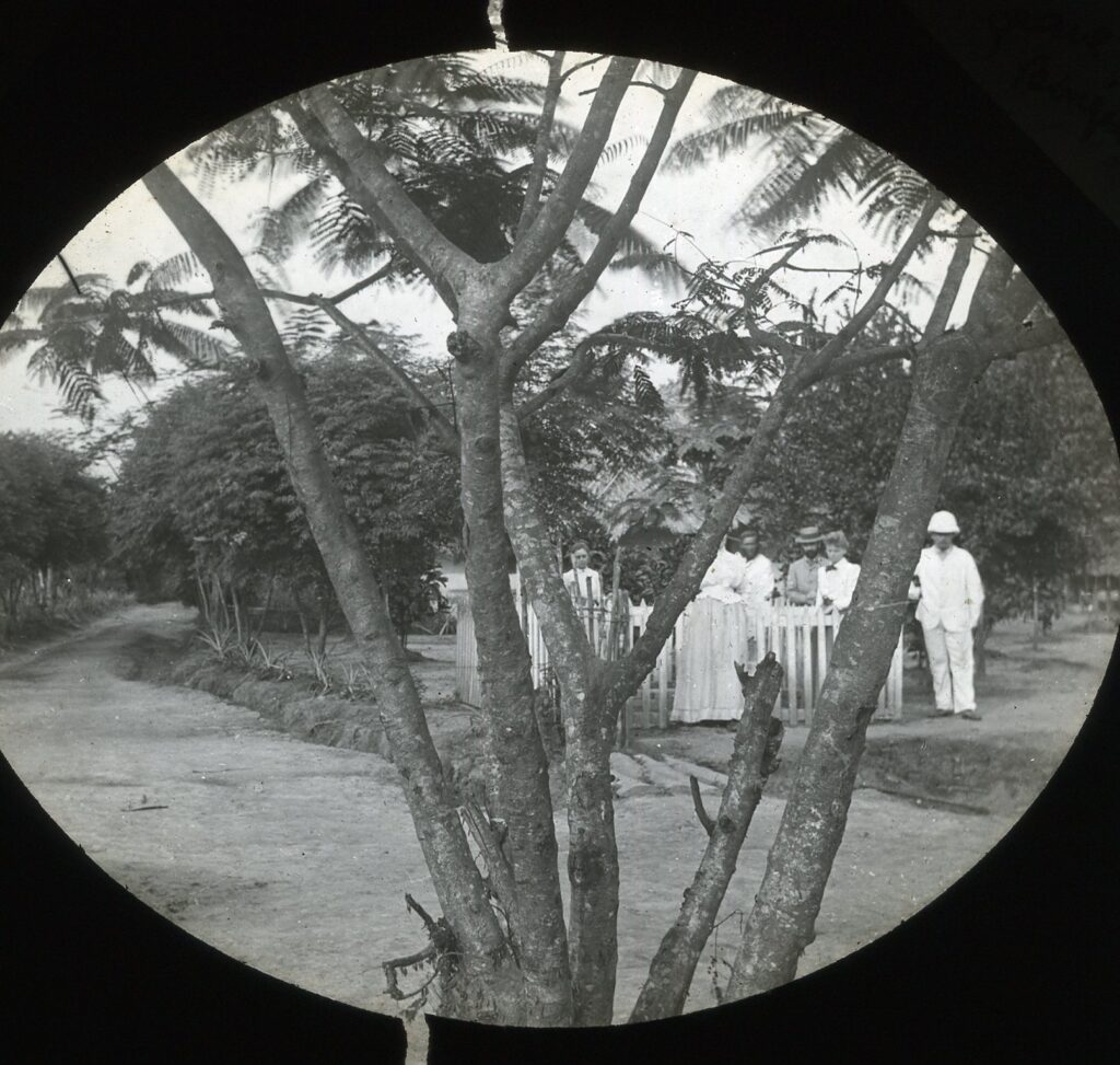 Missionaries gathered around a grave marked by a white picket fence