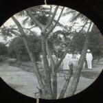 Missionaries gathered around a grave marked by a white picket fence