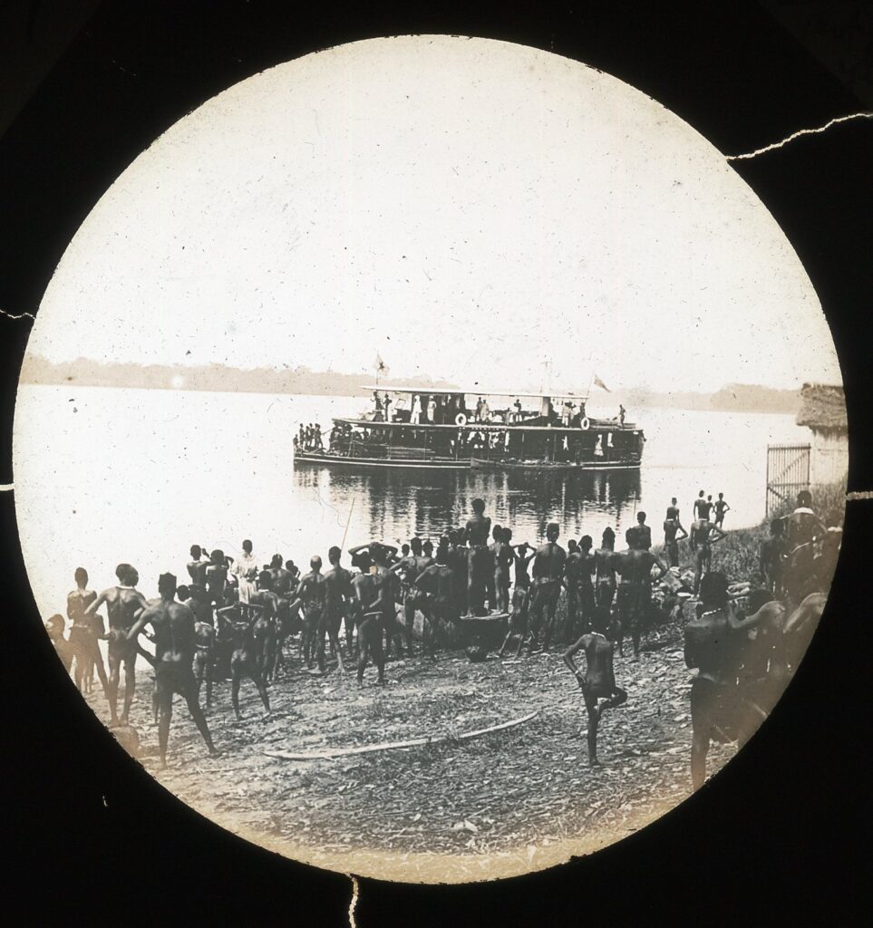 A paddle-steamer ship leaving with locals assembled on the riverbank