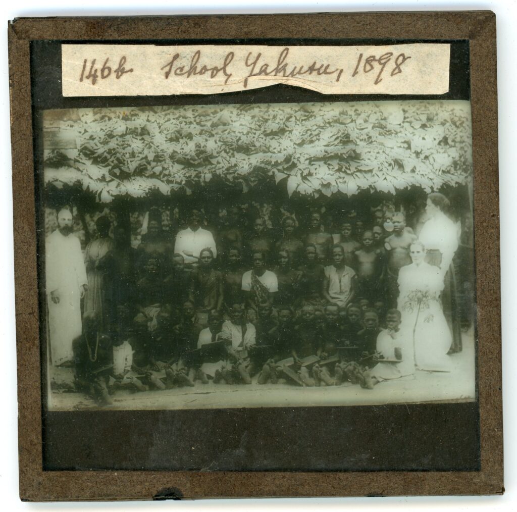 Local children and missionaries assembled under a school hut