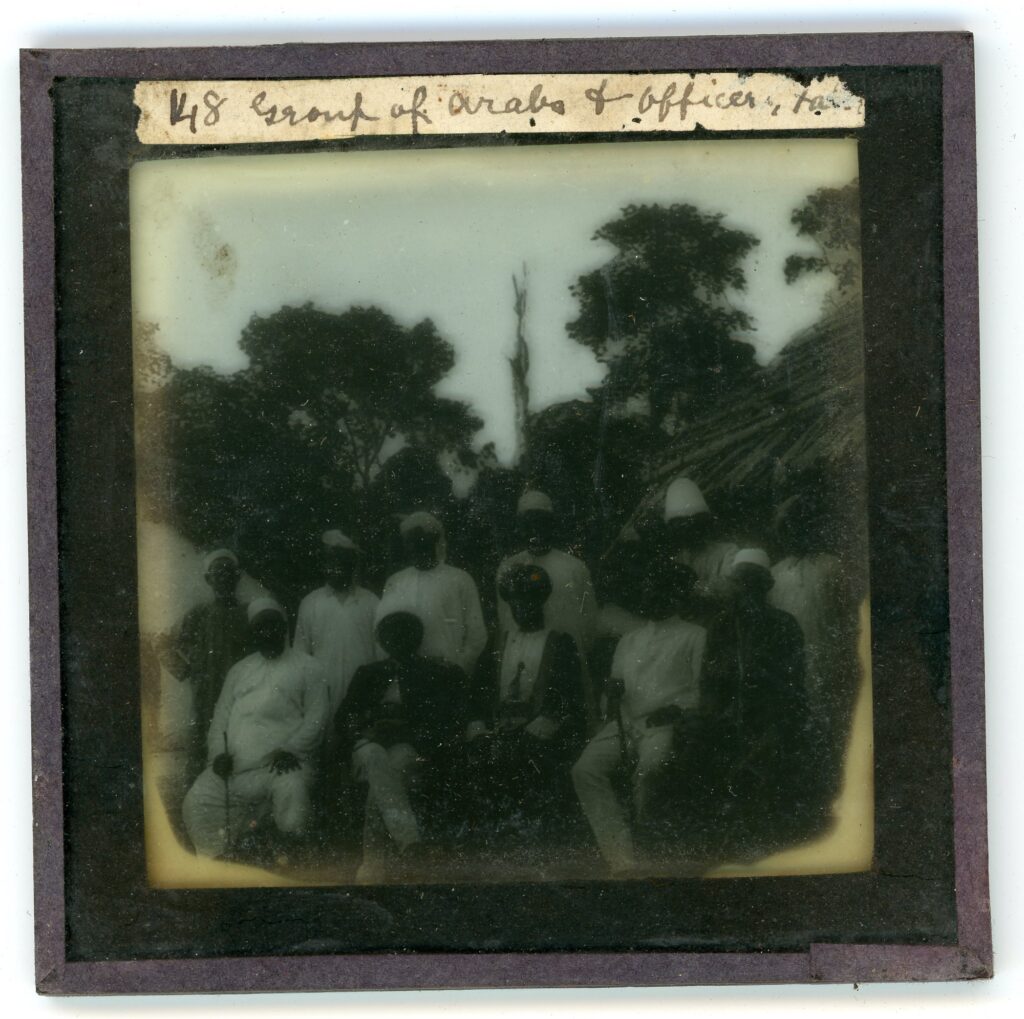 A group of Arabs, missionaries and State officials assembled in front of a hut