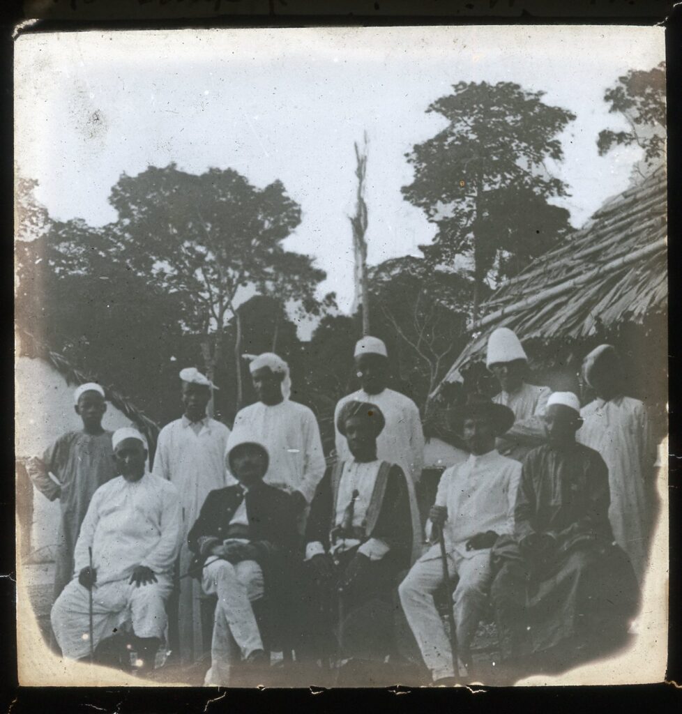 A group of Arabs, missionaries and State officials assembled in front of a hut