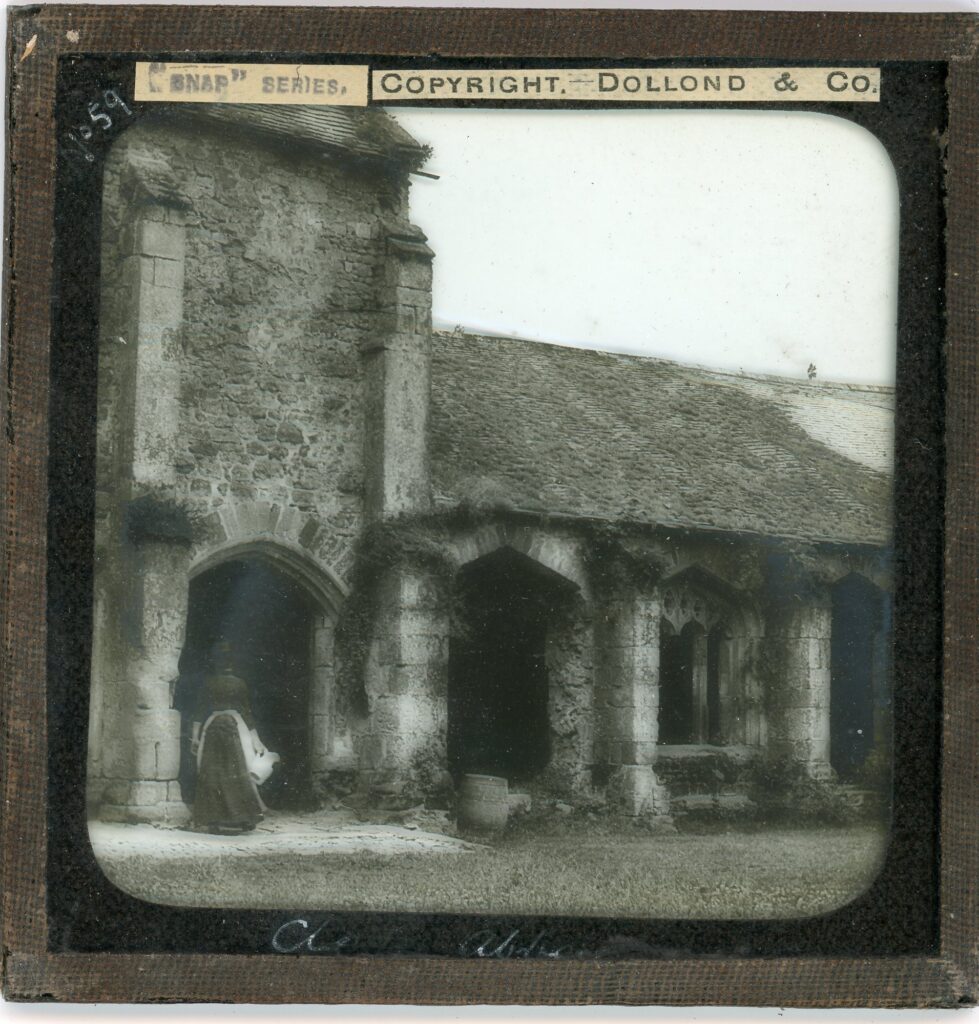 Slide showing a view of a typical English gothic church, slightly overgrown, with a woman in Edwardian dress entering