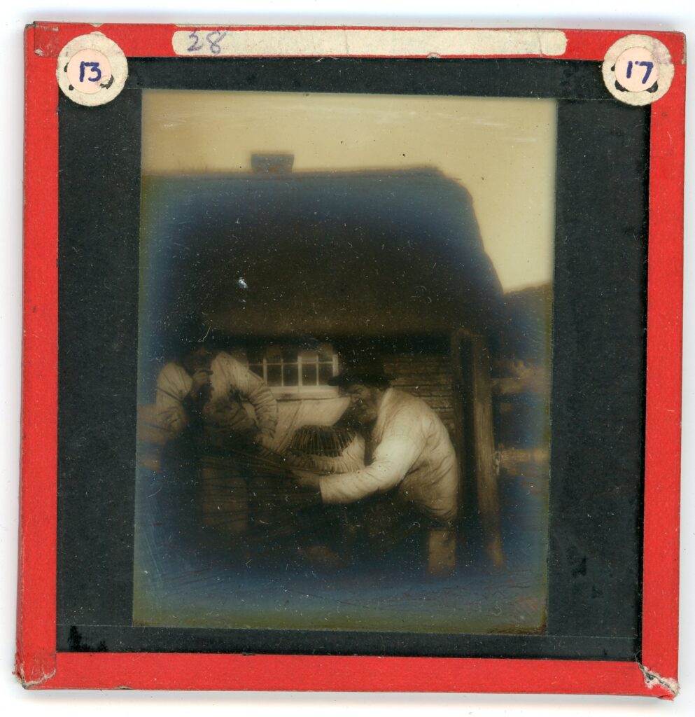 Slide showing two Cornish farmers weaving baskets from branches of wood in front of a thatched roof cottage