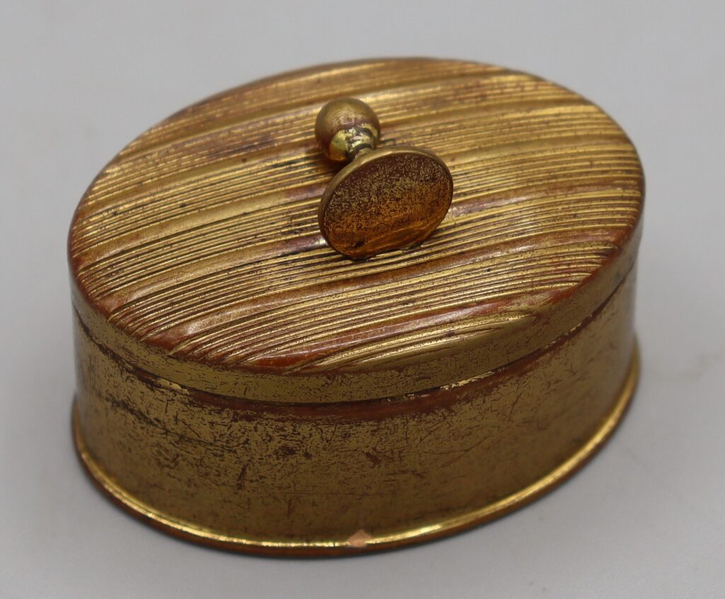 Gold tone metal oval box shown closed, front view