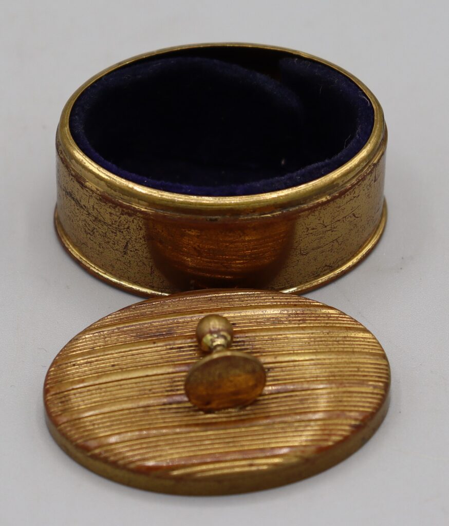 Gold tone metal oval box, shown with lid removed and placed in front of the box